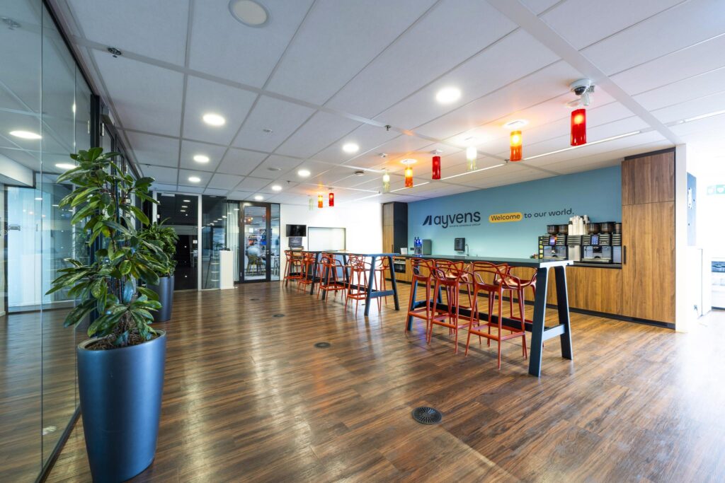 Moderne bedrijfsruimte aan de Johan Huizingalaan met een koffiehoek, hoge zitbanken en kleurrijke verlichting bij Ayvens.